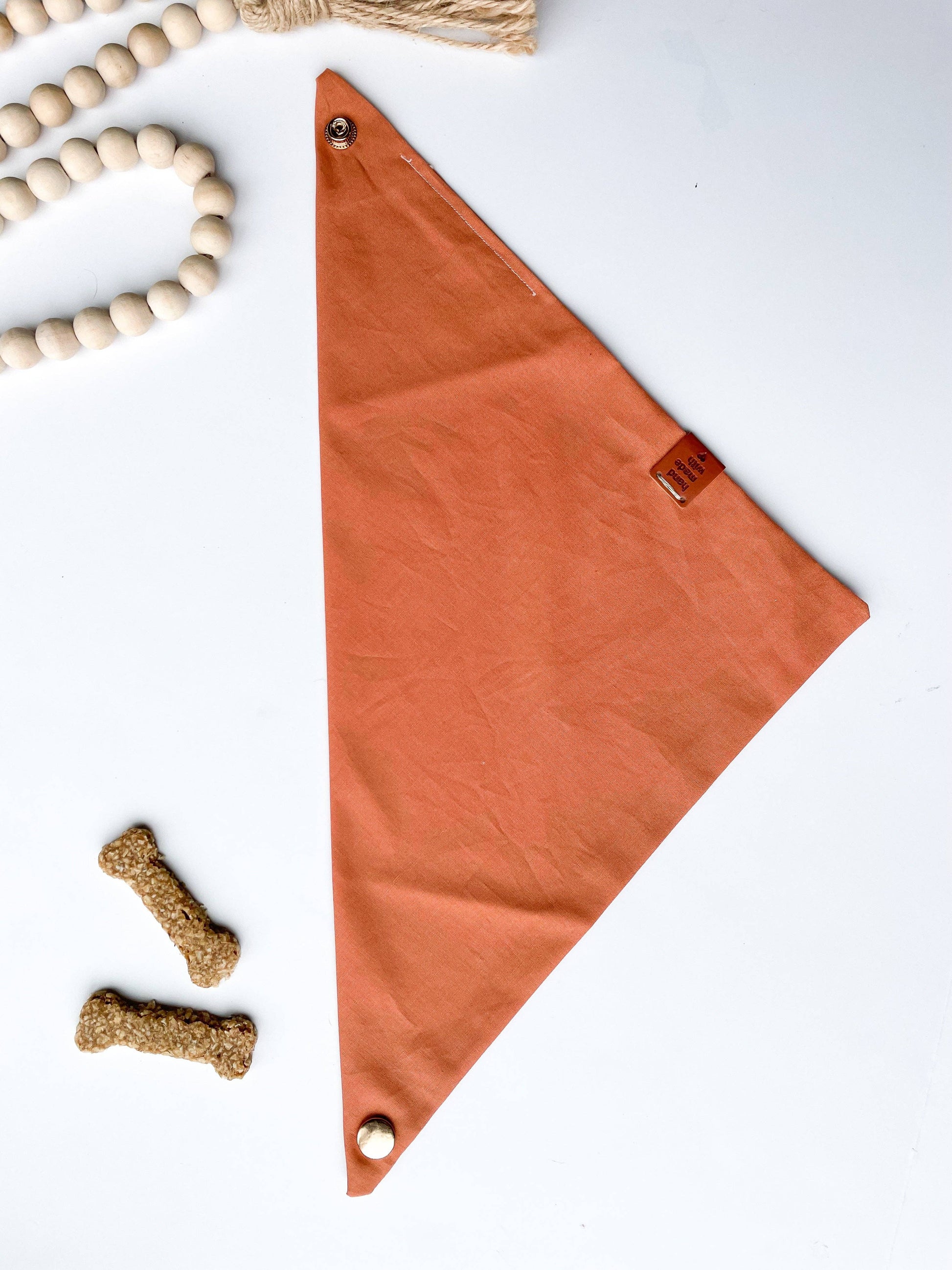 Citrus bandana unfolded on white background. Dog treats on lower left corner, off white beads on upper left corner