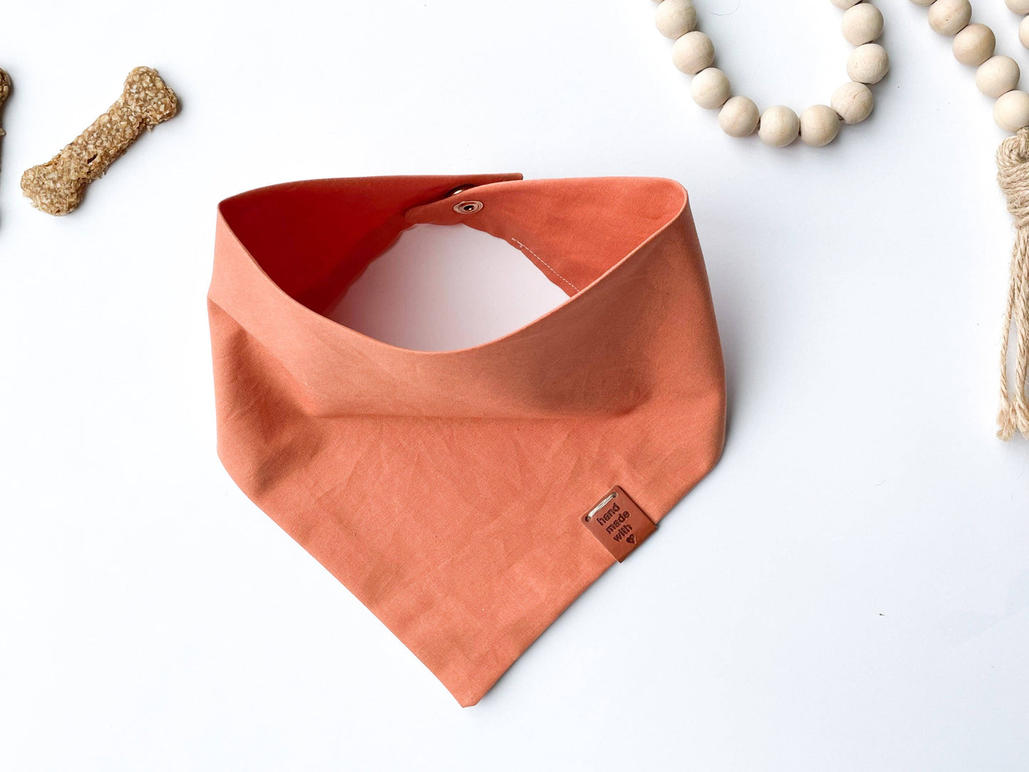 Citrus bandana on white background. Dog bone on upper left corner, off white beads in upper right corner